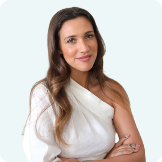 A woman with long brown hair, wearing an off-shoulder white top, smiles confidently with her arms crossed against a light background, representing a social media scheduler | plannthat.com