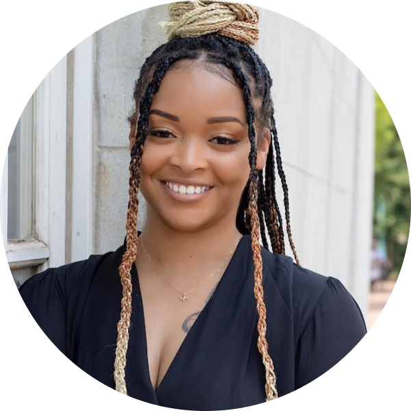 A woman with braided hair and a black top smiles, standing outdoors near a wall, showcasing her role as a social media planner | plannthat.com